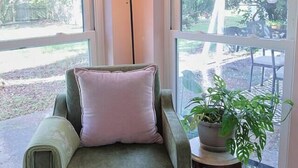 Una habitación con un sillón verde, una pequeña mesa con una planta en maceta y un ventanal con vistas al exterior.