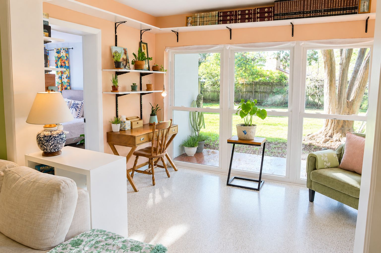 Una habitación con escritorio, silla, estanterías con plantas, una ventana con vistas al exterior y un sofá verde.