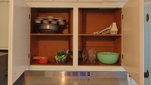 Un meuble de cuisine avec des étagères contenant des casseroles, un pichet doseur, un saladier vert et un jouet.