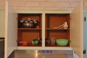 Un meuble de cuisine avec des étagères contenant des casseroles, un pichet doseur, un saladier vert et un jouet.