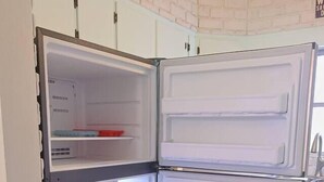 Un réfrigérateur blanc, doté de plusieurs étagères et d’un compartiment congélateur, se trouve dans une cuisine aux meubles blancs et au sol à motifs.