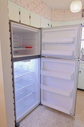 Un réfrigérateur blanc, doté de plusieurs étagères et d’un compartiment congélateur, se trouve dans une cuisine aux meubles blancs et au sol à motifs.