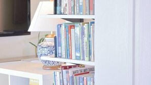 Una estantería con varios libros y un televisor al fondo.