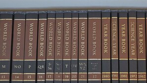 Une rangée de livres à couverture rigide intitulés « WORLD BOOK » et « YEAR BOOK », avec des étiquettes bien visibles sur le dos et les années de publication.