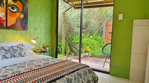 A bedroom with a bed, a nightstand, a lamp, a colorful rug, and a view of a garden through a sliding door.