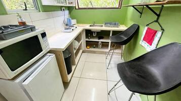 A compact kitchen with a microwave, sink, and a small dining area with a chair.