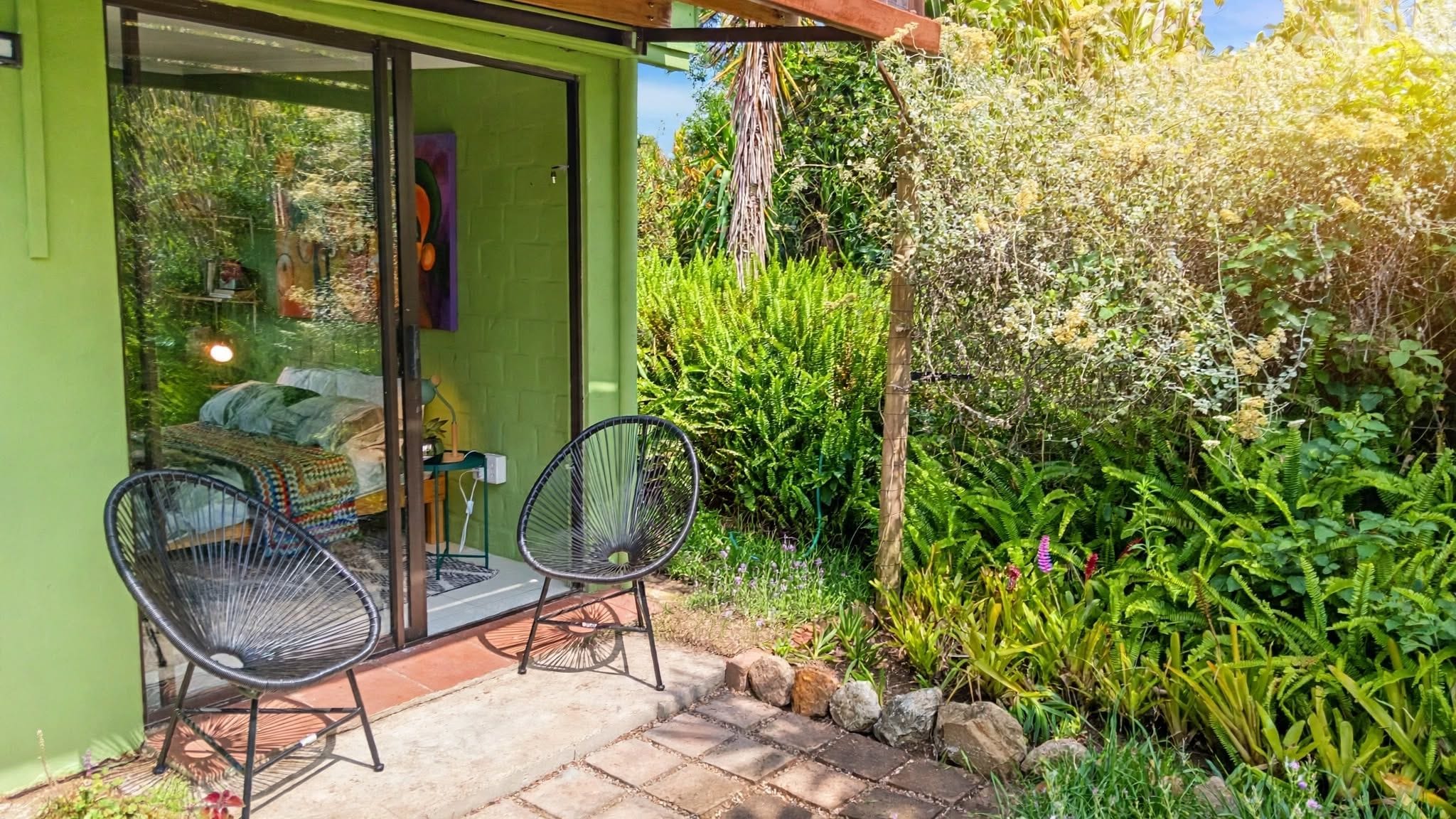 A green house with a glass door leading to a bedroom with a bed and two chairs outside.
