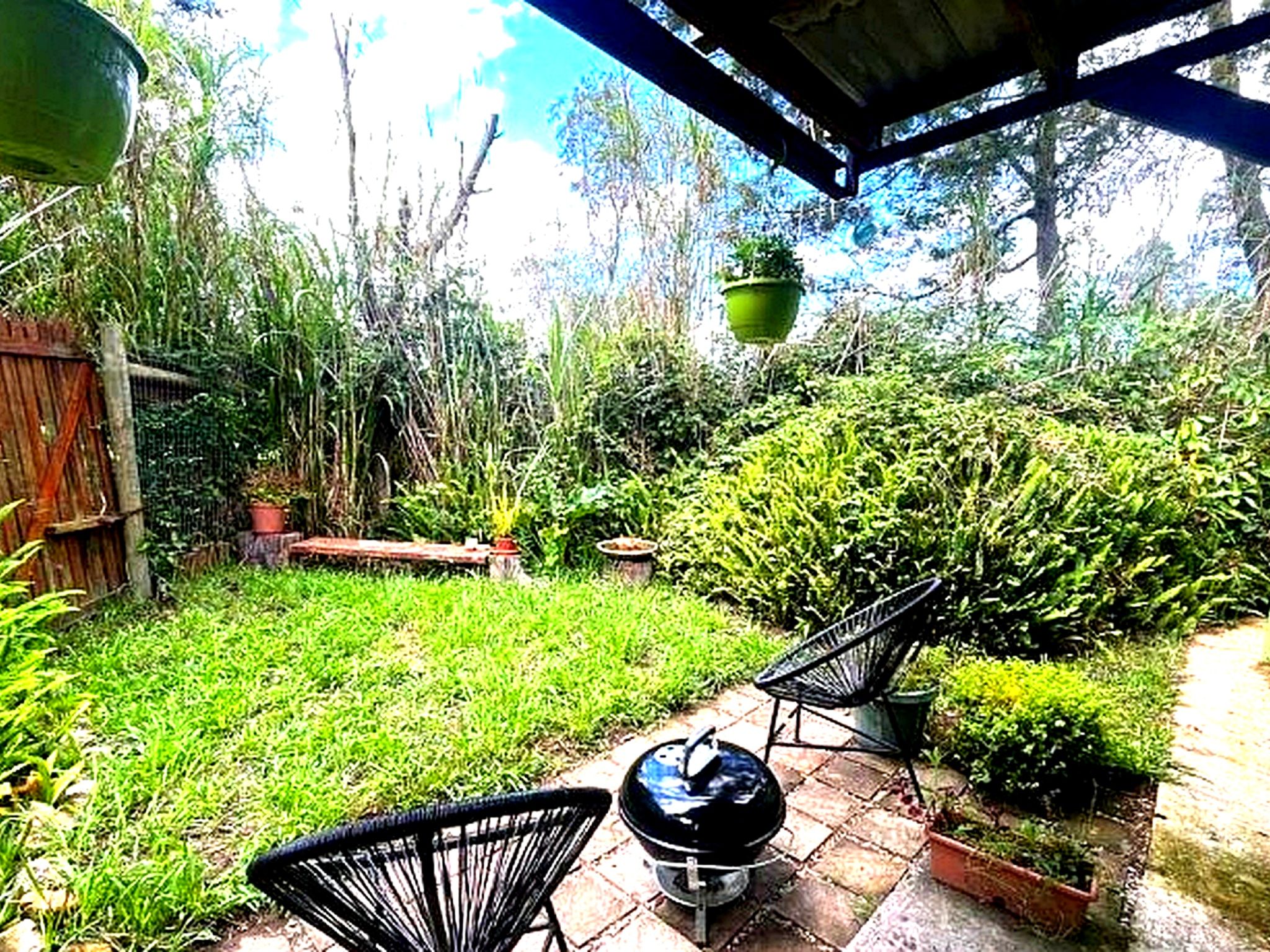 A patio with a grill, chairs, and a hanging planter.