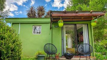 A green house with a sliding glass door, two chairs, a barbecue grill, and hanging planters.