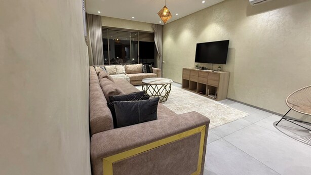 A modern living room with a sofa set, a coffee table, a TV, and a wall-mounted air conditioner. - Elegant Stay - Les Acacias - Guéliz City Center (Marrakesh)