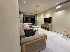 Ein modernes Wohnzimmer mit einer Sofagarnitur, einem Couchtisch, einem Fernseher und einer Wand-Klimaanlage.