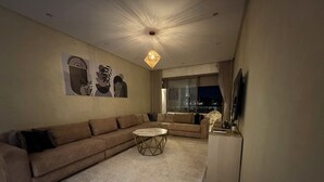 A modern living room with a sectional sofa, a round coffee table, and a wicker chair. - Elegant Stay - Les Acacias - Guéliz City Center (Marrakesh)
