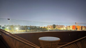 A balcony with wicker chairs and a glass table, overlooking a cityscape at dusk. - Elegant Stay - Les Acacias - Guéliz City Center (Marrakesh)