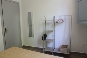 Ein Zimmer mit einem Bett, einem Kleiderschrank, einem Spiegel und einem Metallregal mit Kleidung.