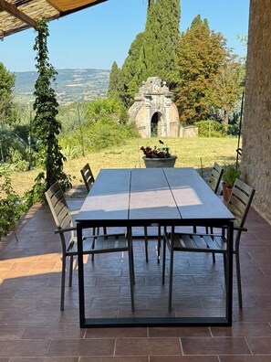 A covered patio with a table and chairs, a stone archway, and a view of the countryside. - HOUSE OF CONSOLATION Small villa adjacent to the Temple of Consolation (Todi)