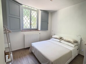 A bedroom with a bed, a radiator, a window with shutters, and a ladder. - HOUSE OF CONSOLATION Small villa adjacent to the Temple of Consolation (Todi)