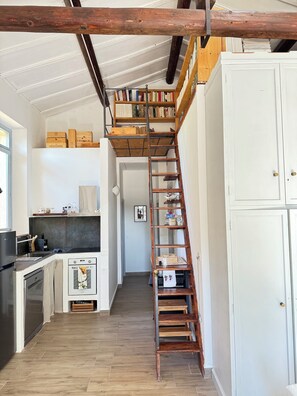 Eine Küche mit einer Holztreppe, die zu einem Schlafzimmer auf dem Zwischenboden führt, einem weißen Schrank und einem Holzboden.