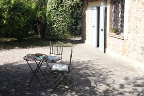 An outdoor seating area with a metal table and chairs, a small table with a plate and a glass, and a stone wall with a door. - HOUSE OF CONSOLATION Small villa adjacent to the Temple of Consolation (Todi)