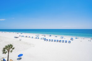 Ein Strand mit weißem Sand, klarem, blauem Wasser und blauen Sonnenschirmen.