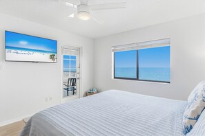 Ein Schlafzimmer mit einem Bett, einem Fernseher, einem Deckenventilator, einem Fenster mit Meerblick und einer Tür zu einem Balkon.