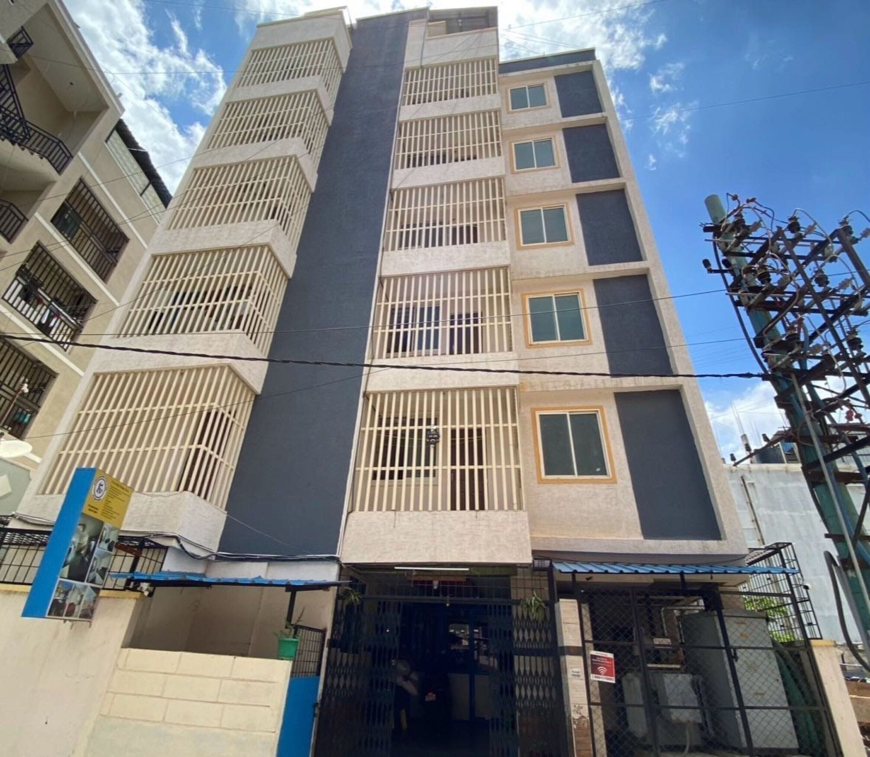 A multi-story residential building with barred windows, a gated entrance, and a visible signboard.
