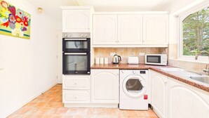 Una cocina compacta con armarios blancos, horno empotrado, microondas, tostadora y lavadora.