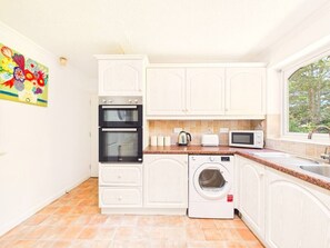Una cocina compacta con armarios blancos, horno empotrado, microondas, tostadora y lavadora.