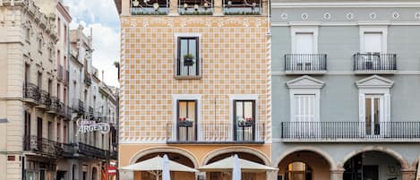 Um edifício com fachada estampada, várias varandas e área externa com mesas e guarda-sóis.
