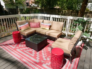 Eine Terrasse mit einer Eckcouch, zwei Beistelltischen und einem gemusterten Teppich.
