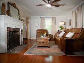 A living room with a fireplace, a clock, a ceiling fan, a brown leather sofa, and a wooden coffee table. - Quiet Forest Hill/Restaurant/James River/Byrd Park (City of Richmond)