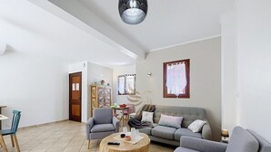 Een woonkamer met een grijze bank, een ronde houten salontafel en een eethoek met een tafel en stoelen.