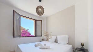 Een hotelkamer met een bed, een raam met gordijnen, een nachtkastje met een lamp en een wandlamp.