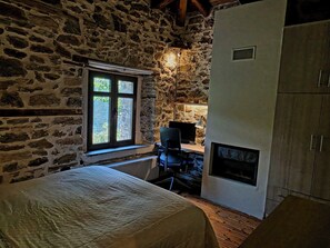 Une pièce aux murs de pierre, avec un lit, un bureau doté d’un ordinateur et une cheminée.