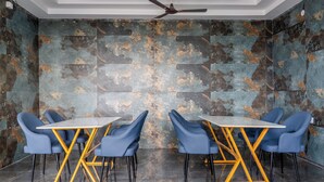 A modern conference room with a ceiling fan, marble walls, and blue chairs around a central table. - Zipp Lite Ballari Leela Hotel & Banquets (Ballari)