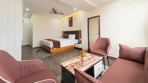 A hotel room with a bed, a desk, two chairs, a ceiling fan, and a door.