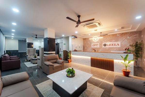 A modern lobby with a reception desk, seating area, and ceiling fans.