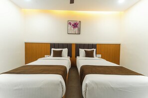 Quarto de hotel com duas camas de solteiro, cabeceira de madeira, obra de arte na parede e teto branco.