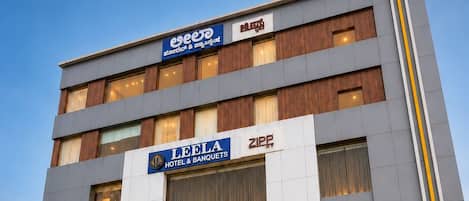 Un hotel LEELA de diseño moderno, con una entrada destacada, varios pisos y un cielo despejado al fondo.