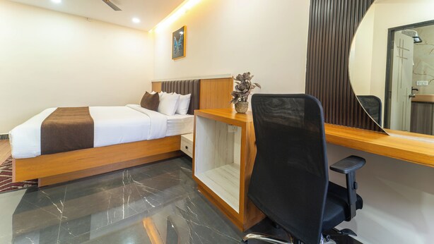 A hotel room with a bed, desk, chair, and a large mirror. - Zipp Lite Ballari Leela Hotel & Banquets (Ballari)
