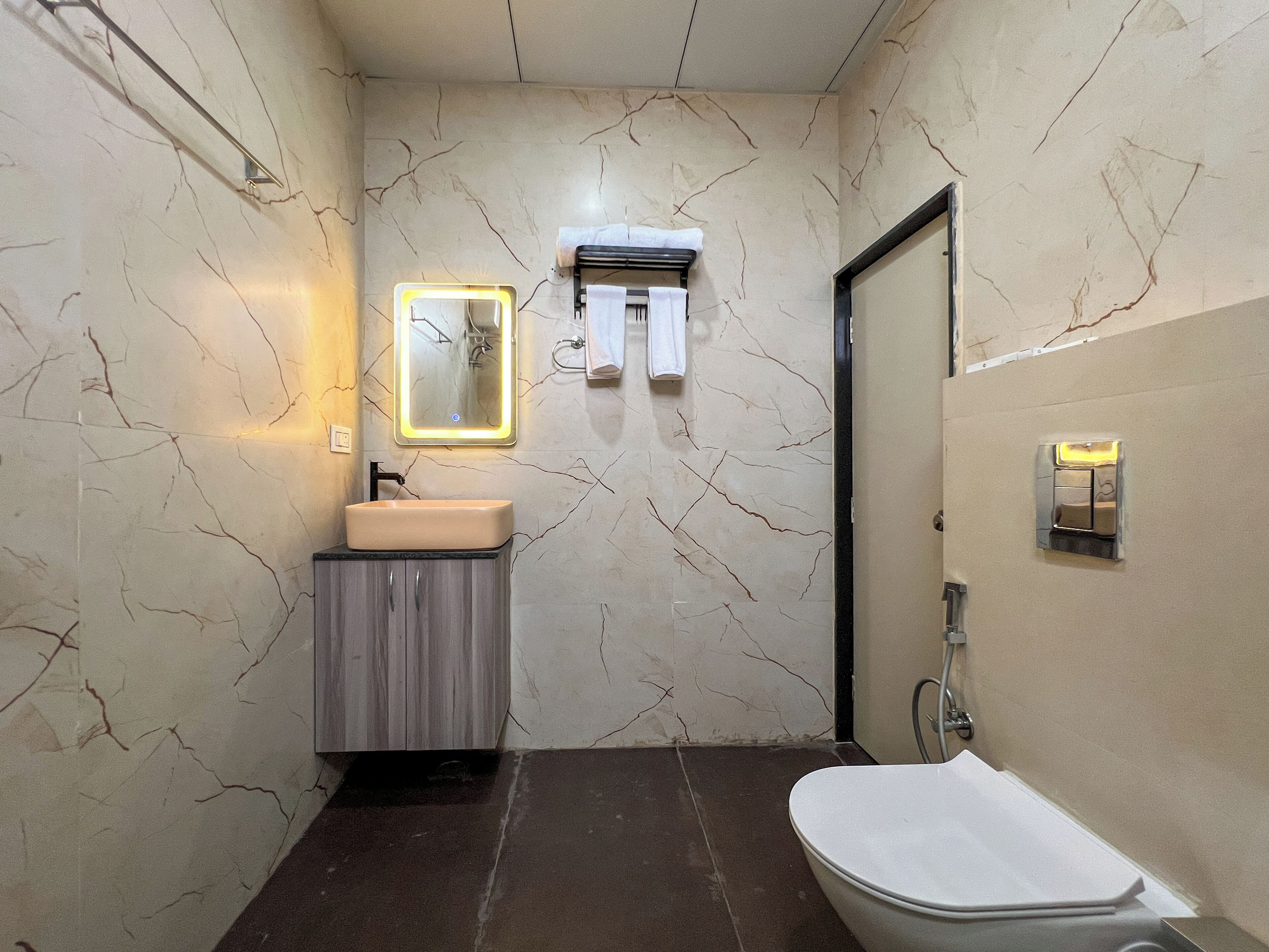 A bathroom with a marble wall, a sink, a mirror, a towel rack, and a toilet.