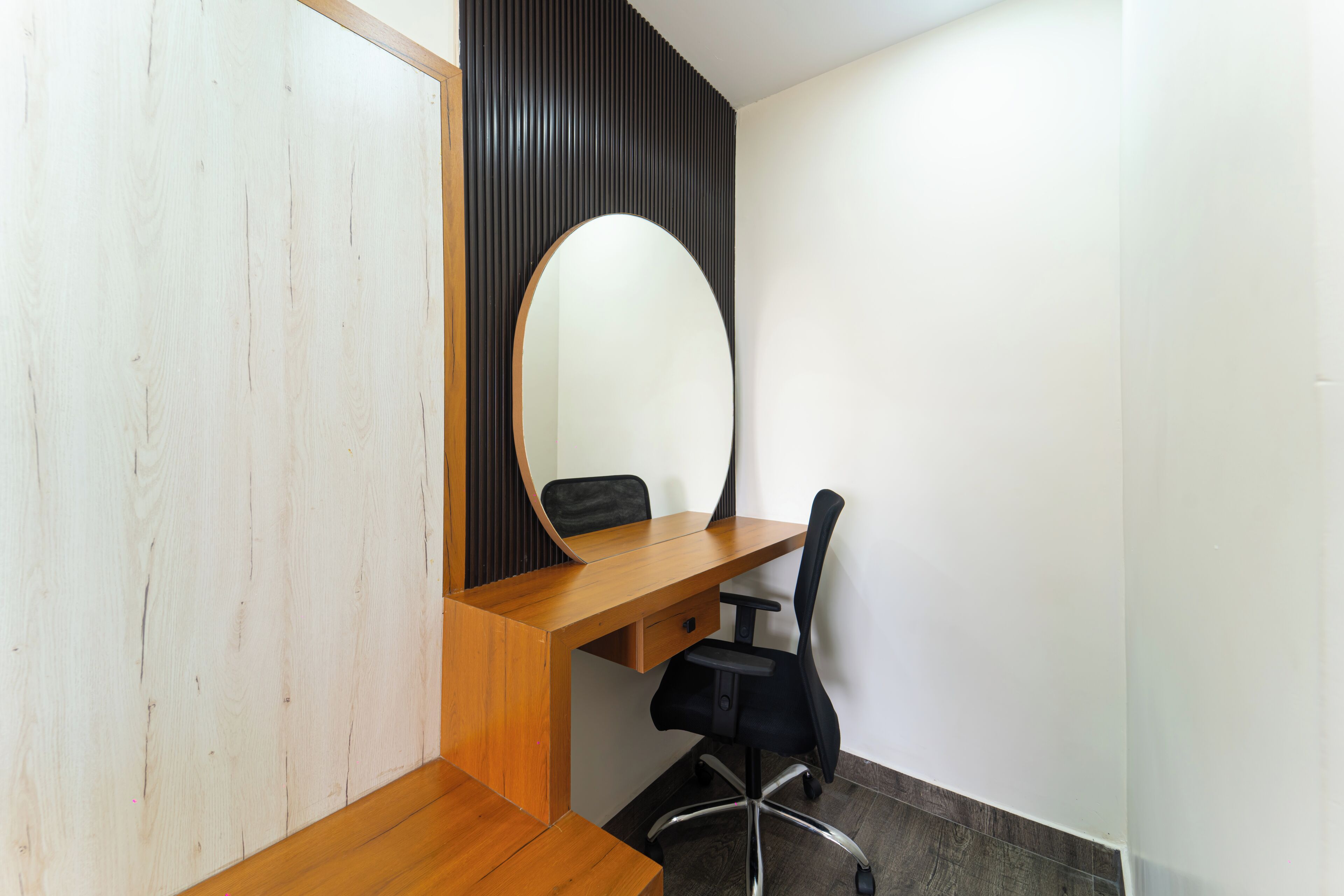 A room with a wooden desk, a black office chair, and a large mirror.