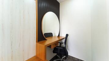 A room with a wooden desk, a black office chair, and a large mirror.