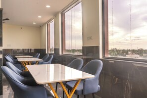 Uma sala de jantar moderna com mesas, cadeiras, grandes janelas e vista para a cidade.