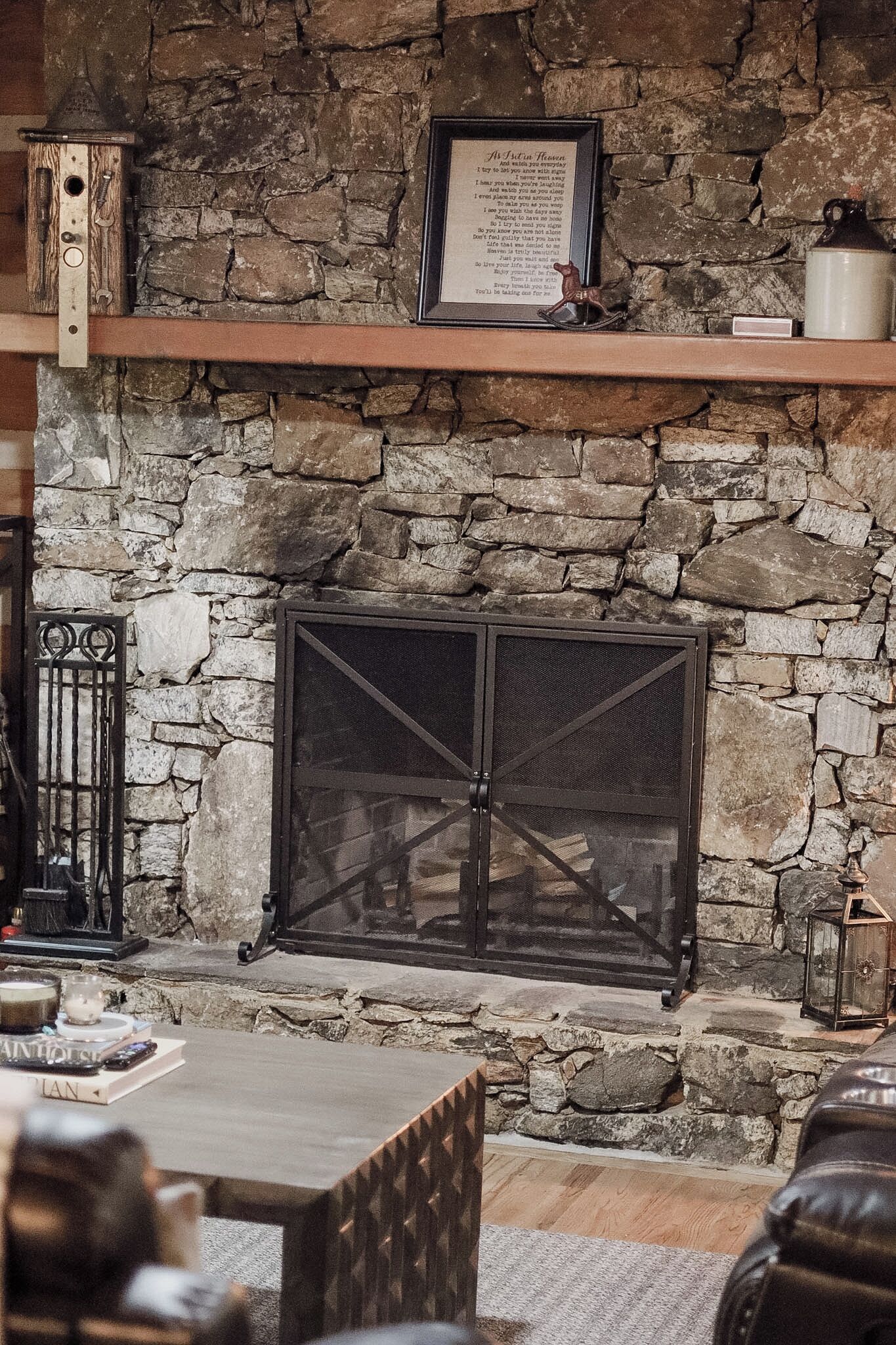 A stone fireplace with a metal screen, a framed poem above it, and a rustic wooden shelf.