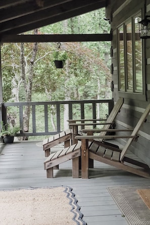 A wooden deck with a bench and a chair, a hanging planter, and a view of trees. - Cozy Cabin- Pisgah Forest, Trails, Waterfalls, River, Brevard & Asheville (Mills River)