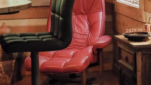 Een houten interieur met een rode lederen stoel, een ronde spiegel en een kleine tafel met glazen.
