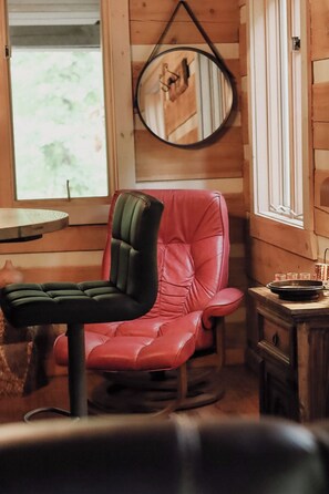 A wooden interior with a red leather chair, a round mirror, and a small table with glasses. - Cozy Cabin- Pisgah Forest, Trails, Waterfalls, River, Brevard & Asheville (Mills River)