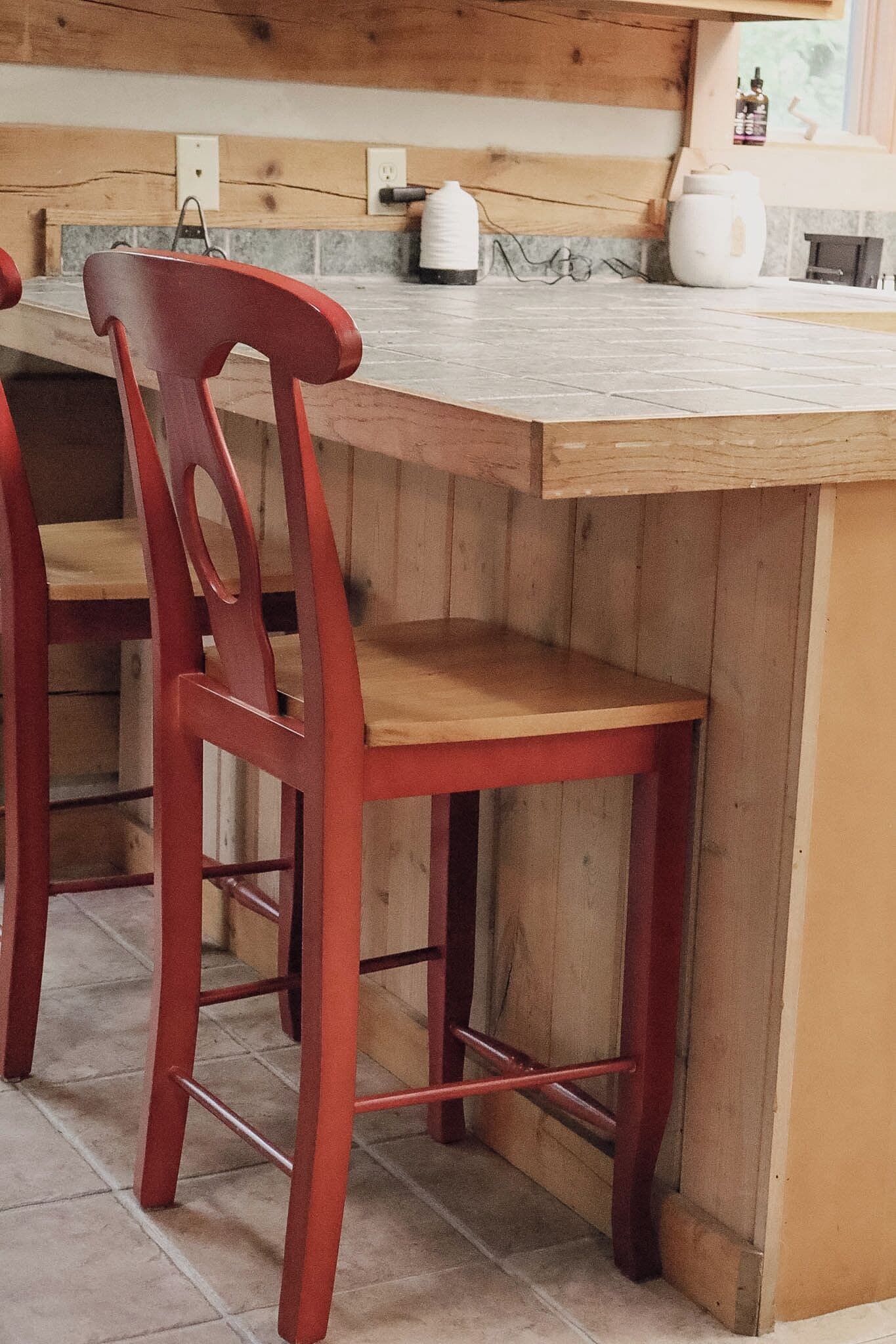 A kitchen with a wooden island, two red chairs, and a white kettle on the counter.
