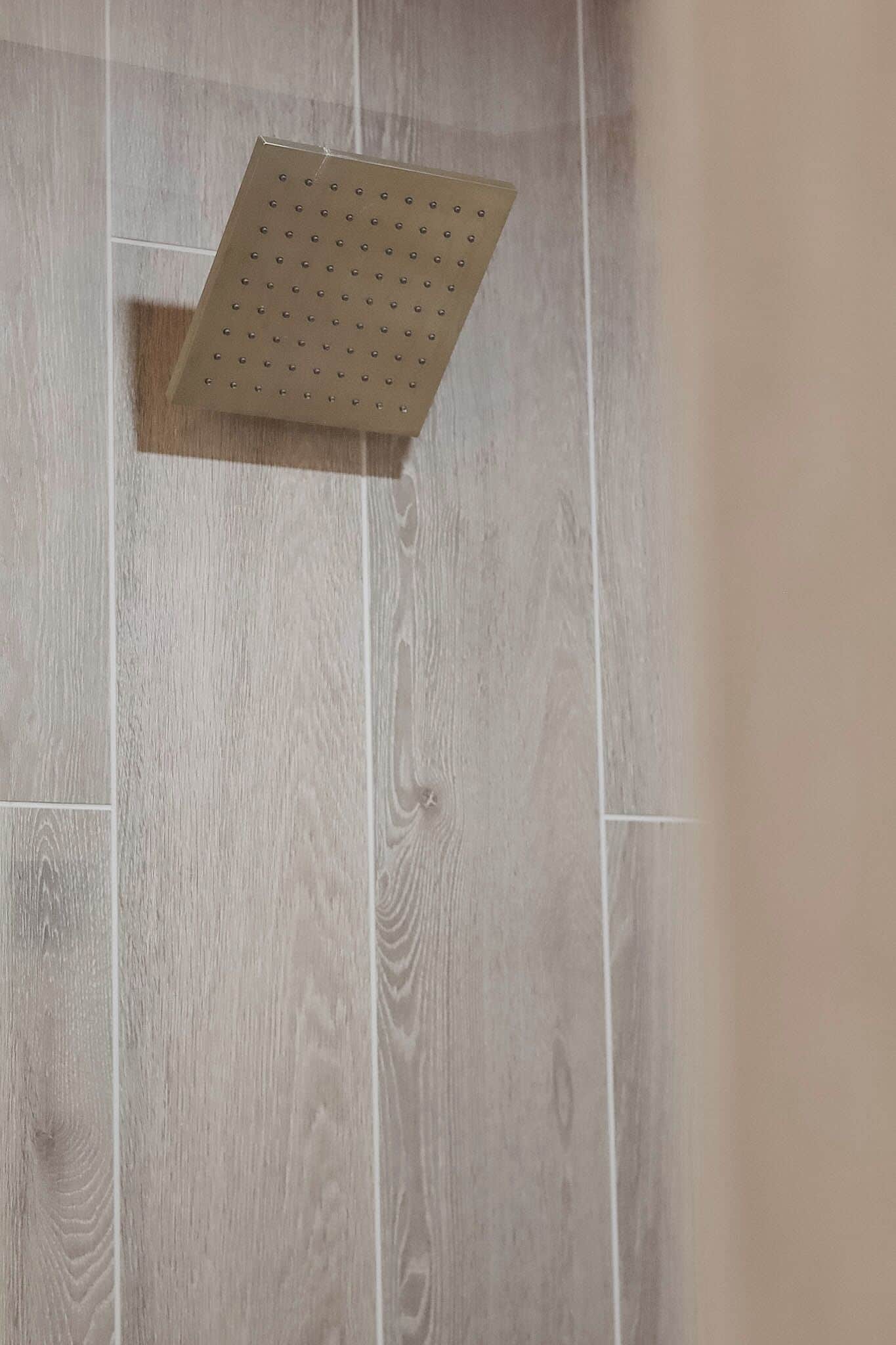 A shower area with a perforated shower head and wooden floor tiles.