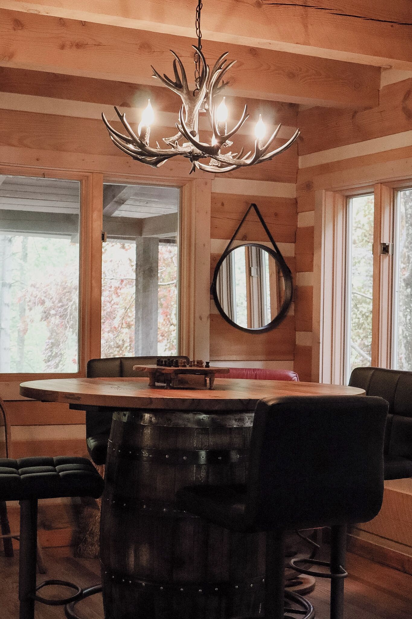 A wooden interior with a chandelier, a round mirror, and a dining table with chairs.